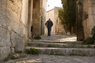 Limestone steps in a narrow Clarensac alley at dawn, a villager walking away with a baguette, golden morning light, wild thyme in stone cracks, and an old iron gate ajar.