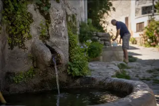 Village fountain with moss and herbs in golden light, villager in background refilling a jug, evoking daily life in a Gard village